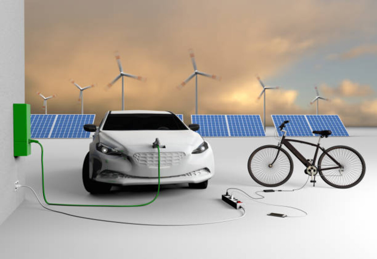 An electric car, an electric bicycle and a mobile phone charge their batteries. Solar panels and wind turbines are in the background. Brandless car. No real prototype.